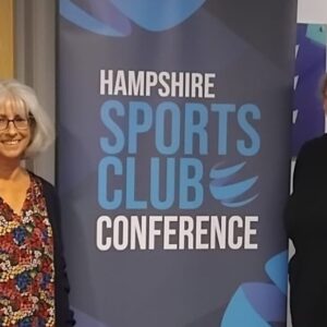Two women, both with glasses, stood beside a placard 'Hampshire Sports Club Conference'
