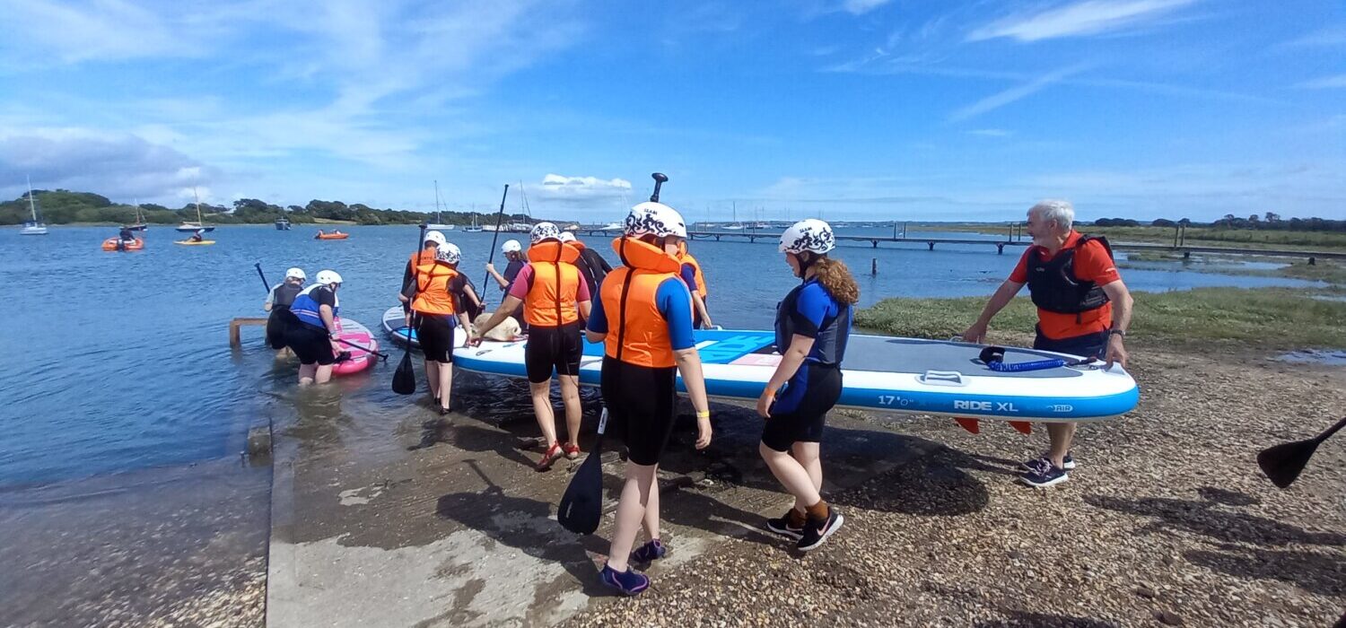 A group of people putting a large paddle board in the water.