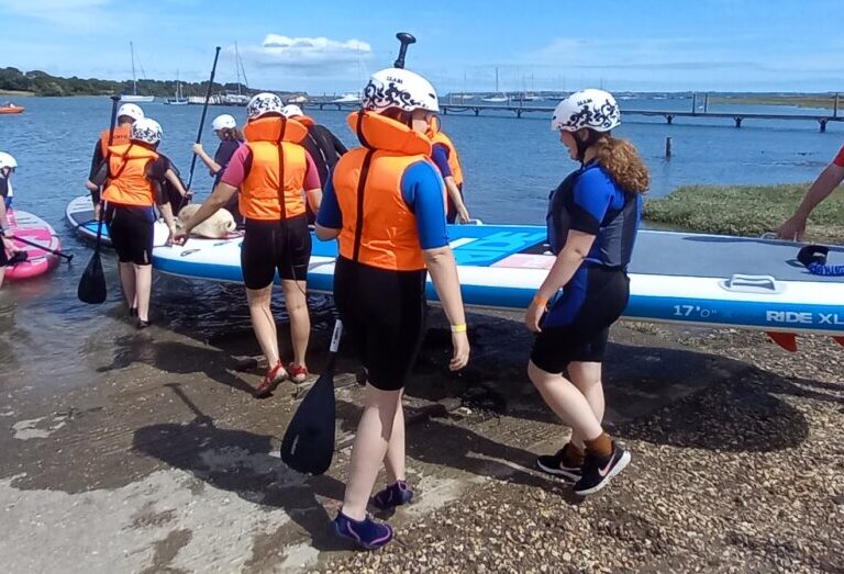 A group of people putting a large paddle board in the water.
