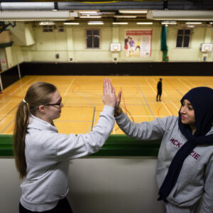 Two girls high-fiving. They're in a gymnasium.