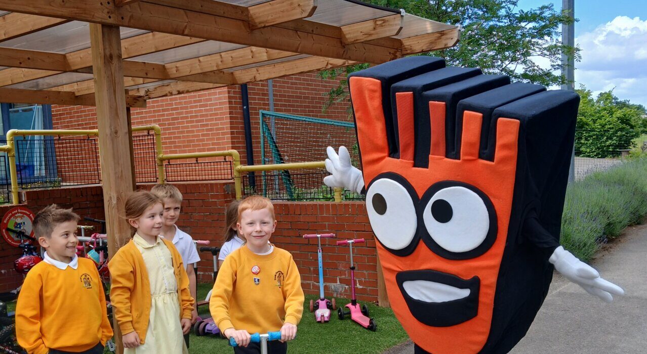 Young children with a scooter next to the bright orange living streets mascot
