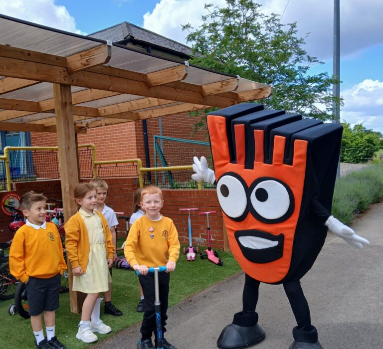 Young children with a scooter next to the bright orange living streets mascot